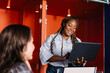 © Adrian Rodd/Stocksy - Diverse woman guiding a team discussion in a tech company