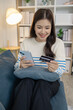 © PHOTO4U - A young woman is sitting on a sofa holding a smartphone and credit card, smiling as she makes an online transaction. She looks relaxed and confident while shopping at home.