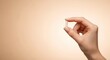 © ENDRA - A persons hand holds a single white pill between thumb and forefinger against a soft, warm, gradient background