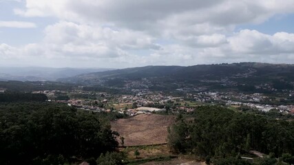 Wall Mural - Wide aerial view of Penafiel, a Portuguese city surrounded by hills, forests, and scattered houses under a partly cloudy sky