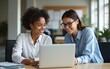 © Betty - Two happy busy female employees working together using computer planning project. Middle aged professional business woman consulting teaching young employee looking at laptop sitting at desk in office