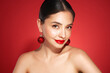 © Oleg Gekman - Portrait of beautiful young woman on red background, red lipstick and festive makeup, Christmas toy earrings, shiny glowing skin, Winter holidays concept