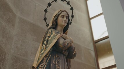 Wall Mural - Close-up of Virgin Mary statue with star halo and folded hands inside church