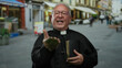 © Krakenimages.com - Senior priest man in street gesturing while holding book in outdoor urban setting, showcasing religious faith and tradition in a vibrant city environment.