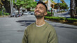 © Krakenimages.com - Young hispanic man smiling on an urban street with trees and buildings in the background, embodying a relaxed and content vibe on a sunny day outdoors.