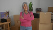 © Krakenimages.com - Senior woman with grey hair crosses arms confidently in a new home's living room filled with cardboard boxes symbolizing moving and change in a modern apartment interior.