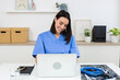 © Xavier Lorenzo - Young female doctor smiling and working on laptop with medical records and stethoscope on desk at clinic