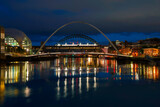 Newcastle city night skyline with Gateshead Millennium Bridge in England. A tranquil riverscape of Quayside with vibrant illuminated water reflections over the River Tyne.