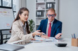 © Tj - Business colleagues are collaborating on data analysis, discussing charts and graphs on printed reports during a corporate meeting in a modern office environment