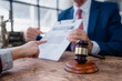 © Tj - Clients and a lawyer are analyzing a legal contract together, pointing to specific clauses on a document with a gavel placed on the rustic wooden table, symbolizing justice and legal agreement