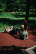 © qunica.com - Two women practicing fitness routines outdoors on a sunny day, performing exercises in a park setting while being fitness-focused and encouraging each other on a red running track.