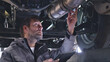 © wkproduction - A mechanic examines a car's exhaust system with a tablet in a well-lit auto shop, emphasizing precision and detail.