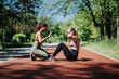 © qunica.com - Two women engage in a fitness session outdoors in a lush park, one performing sit-ups while the other motivates. This sunny scene depicts teamwork, health dedication, and active lifestyles.
