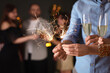 © New Africa - Friends celebrating New Year with sparklers and wine glasses indoors, closeup