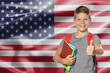 © New Africa - Little boy with backpack and stationery showing thumbs-up against flag of USA. Language school