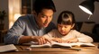 © ON - Studio - A caring Asian father helps his young daughter with her homework at night. Parent and child reading a book together under a desk lamp. Education and family bonding concept