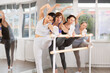 © JackF - Active young adult Asian woman with group of fitness female enthusiasts engaging in modern barre workout, performing stretching exercises, focusing on body flexibility
