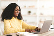 © Prostock-studio - Pretty young black woman in casual employee sitting at worktable with stationery, working on laptop at office, typing on keyboard and smiling, making marketing analysis, copy space
