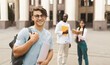 © Prostock-studio - Student guy standing outdoors in campus with his classmates and university building on background, posing and smiling to camera. Higher education concept