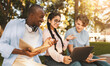© Prostock-studio - Happy diverse students studying together in park, preparing for test and looking at laptop screen, sitting on bench in park or college campus