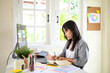 © Prathankarnpap - Female graphic designer sketching logo concepts in a notebook with colored pencils at creative workspace