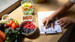 © Prathankarnpap - Nutritionist analyzing and writing a healthy meal plan with fresh fruits, vegetables, and nuts on the table