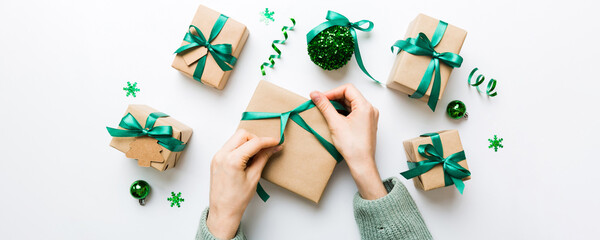 Wall Mural - Woman is packing surprise gift for Christmas holidays, sitting at workplace with craft tools, top view. Woman wrapping Christmas gift at colored table