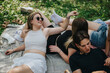 © qunica.com - A group of friends spending time outdoors, lying on a blanket in a park, enjoying sunny weather, and socializing in a cheerful and casual atmosphere.