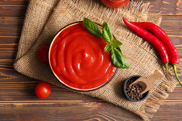 Wall Mural - Bowl of tasty tomato sauce with basil leaves, peppercorns and chili peppers on wooden background