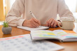 © Nanci - Woman's hands writing notes in a physical planner or journal, organizing daily activities and appointments for improved productivity and a balanced lifestyle at a home office desk