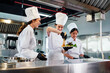 © artitwpd - Team of chefs in white uniforms and toques plate gourmet dish in commercial kitchen. Scene shows instructor-led collaboration, dining presentation, stainless workflow, education, teamwork in school.