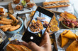 © jcalvera - Hand holding smartphone photographing latin american food sharing