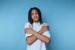 © bodnarphoto - Young man with braided hair hugging himself against a blue background.