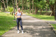 © MINAE - Young Asian woman in sportswear smiling and pointing at the camera on a sunlit park path among lush green trees, radiating energy, motivation and healthy lifestyle appeal