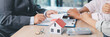 © doidam10 - Mortgage consultation panorama with miniature house model in hand, financial advisor meeting clients, property investment, home loan agreement, real estate planning and housing business negotiation.