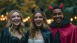 © TrubiAnna - Three diverse friends celebrate Halloween in costumes. A young Caucasian woman with blonde hair, a young Hispanic woman with brown hair, and a young Black man with short hair smile at a party.
