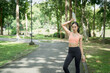 © MINAE - Asian woman standing on park path, raising a water bottle to her head after a run, cooling down and hydrating in activewear amid green trees, focused and refreshed