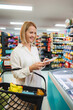 © Jelena - Woman smiling while checking shopping list in supermarket