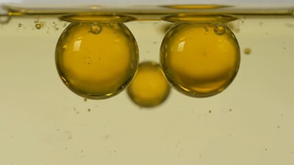 Wall Mural - macro slow motion of golden oil drops gently separating and reforming within a transparent liquid tr