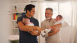 © Monkey Business - Grandfather With Adult Son Holding Twin Baby Granddaughters At Home