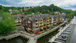 © AmazingAerialAgency - Aerial view of colorful townhouses with intricate architectural details line a waterfront boardwalk, juxtaposed against the lush green trees, Woodbridge, Virginia, United States.