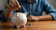 © Item.io - Person dropping a coin into a white piggy bank on a wooden table.