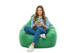 © Thecreator T - A happy woman smiles using phone while sitting on a green beanbag chair in a comfortable and relaxed position on transparent background