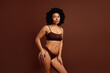 © deagreez - Charming young woman in activewear posing against a solid brown background, symbolizing self-acceptance