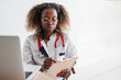 © etonastenka - A black female doctor sits at a laptop and writes down the diagnosis in a notebook. Online doctor's consultation. High quality photo