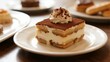 © yanli - A slice of tiramisu dessert topped with whipped cream and cocoa powder, served on a white plate.