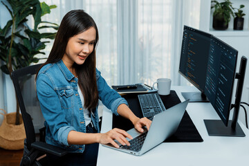 Smiling young Asian in IT developer creating with typing online information on laptop with coding program data of application, wearing jeans shirt. surrounded by safety analysis two screen. Stratagem.