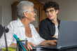 © Светлана Мищенко - Teenage grandson teaching his grandmother to use a laptop at home. Generations learning together, family support, digital literacy for seniors, technology, connection, love, and intergenerational care