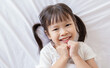 © paulaphoto - Portrait adorable little girl with pigtails smile brightly while lying on a white bed in a cozy cheerful home environment. Education preschool toddler.