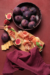 Wall Mural - Wooden board of bread slices with delicious prosciutto and fresh fig on red background